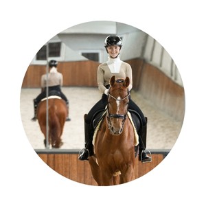 Kim Burschik est assise sur son cheval dans le manège et sourit.